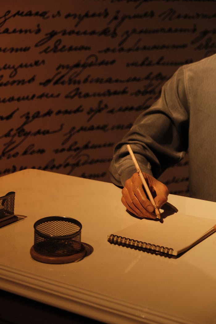 Close-up of hand writing at a desk with vintage decor and warm lighting.