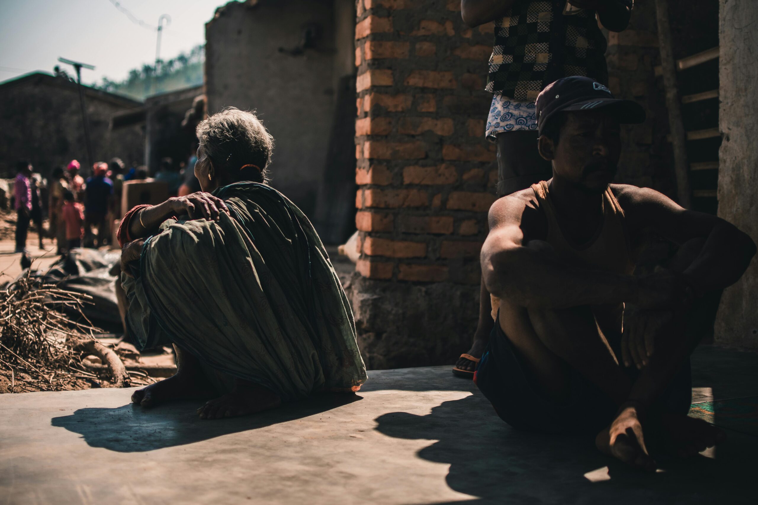 Why Bahujan is Not United and What Must Change A group of adults sitting outdoors in a village setting, casting strong shadows on a sunny day.